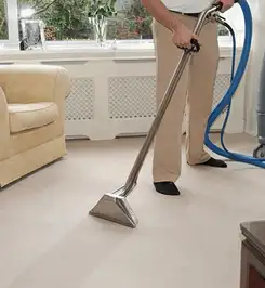 Professional carpet cleaner using a hot-water extraction wand and hose machine in a living room in Baltimore, MD.