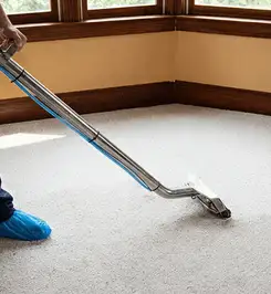 Steam carpet cleaning technician using a hot-water extraction wand on a residential carpet, wearing blue protective shoe covers Baltimore, MD.