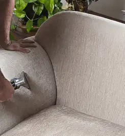 Professional upholstery cleaner deep-cleaning a fabric sofa with a handheld extraction tool and hose Baltimore, MD.