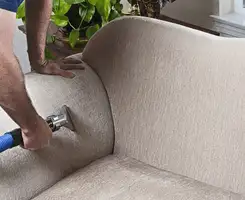 Professional upholstery cleaner deep-cleaning a fabric sofa with a handheld extraction tool and hose in Baltimore, MD.
